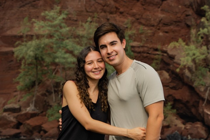 Couple posing in front of red cliff and blue water.