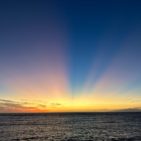 Sunset over ocean with vibrant rays in a clear sky.