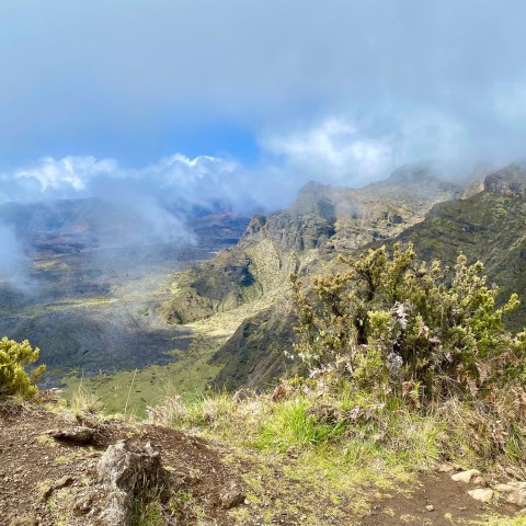 Mountain landscape with rocky cliffs and patches of greenery under a cloudy sky.