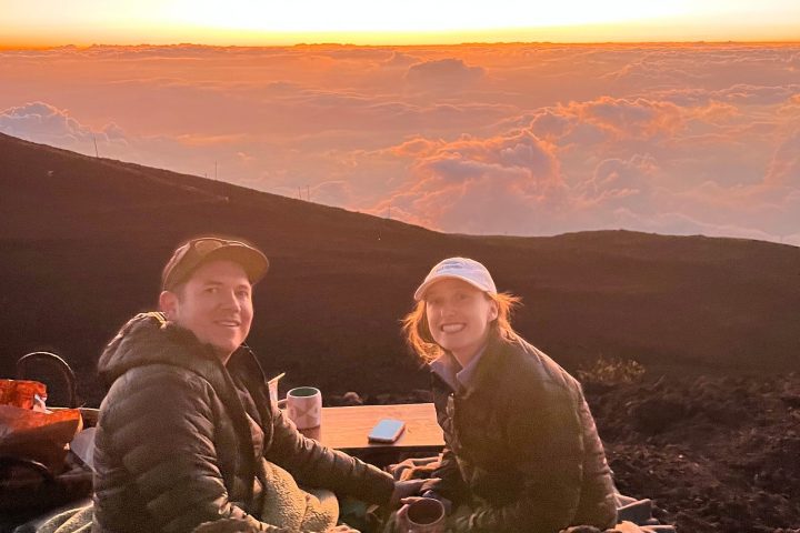Two people enjoying a sunset view from a rocky hilltop.