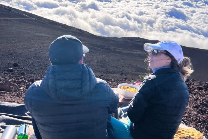 Two people sitting on a mountain slope with a vast cloudscape view.