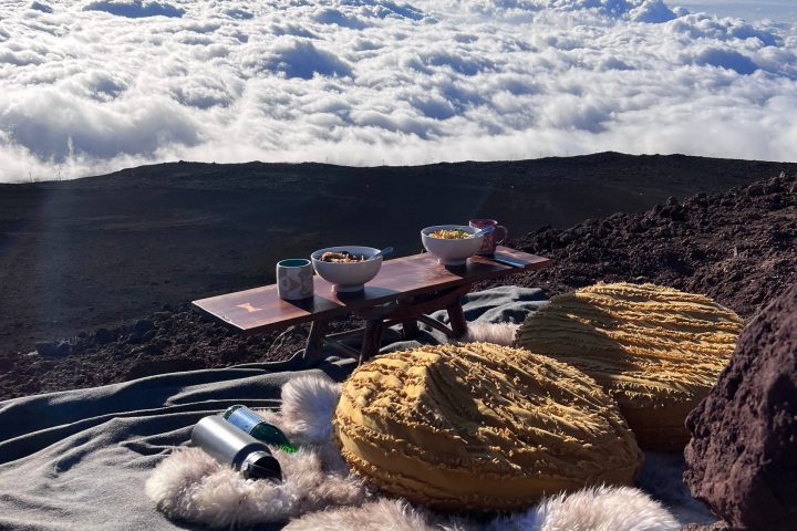 Cloudy mountain view with picnic setup of cushions, blankets, and drinks.