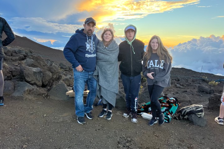 Four people stand on a rocky hilltop at sunset, wrapped in warm clothing.