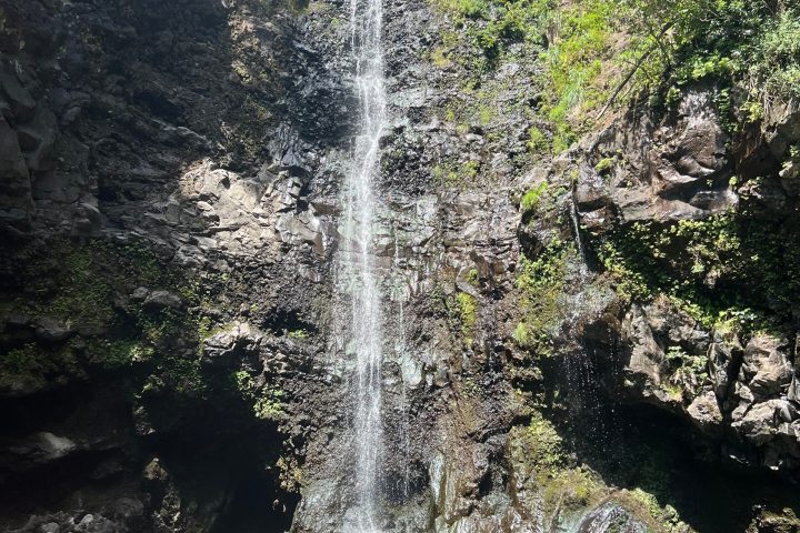 Tall waterfall cascading down rocky cliff into a green pool.