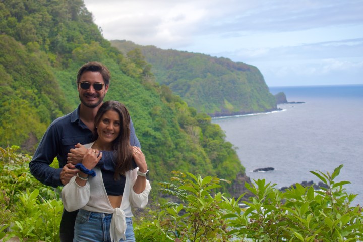 Smiling couple posing near lush cliffs overlooking the ocean.
